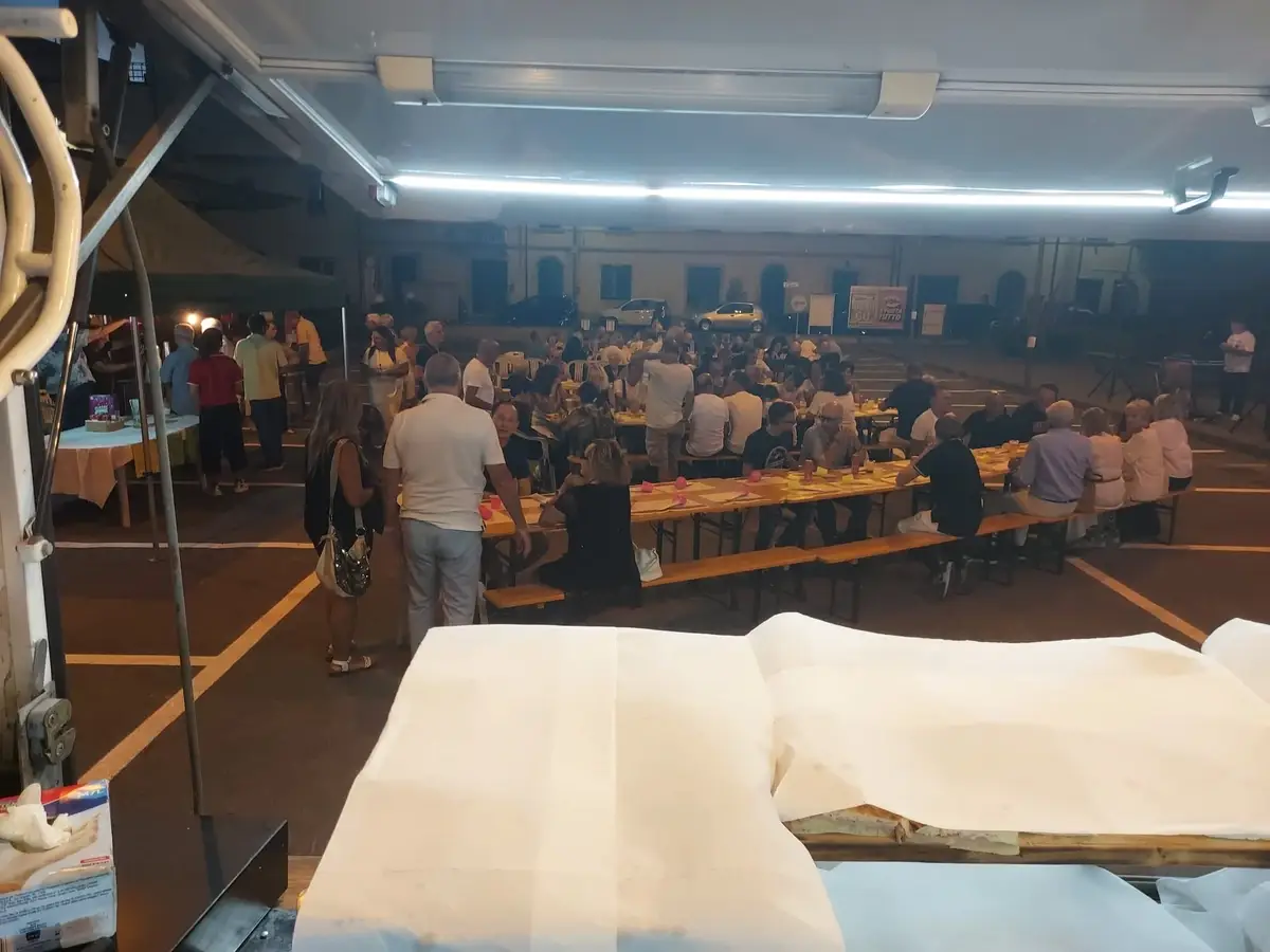 La piazza con i tavoli lunghi apparecchiati e la gente seduta, di sera