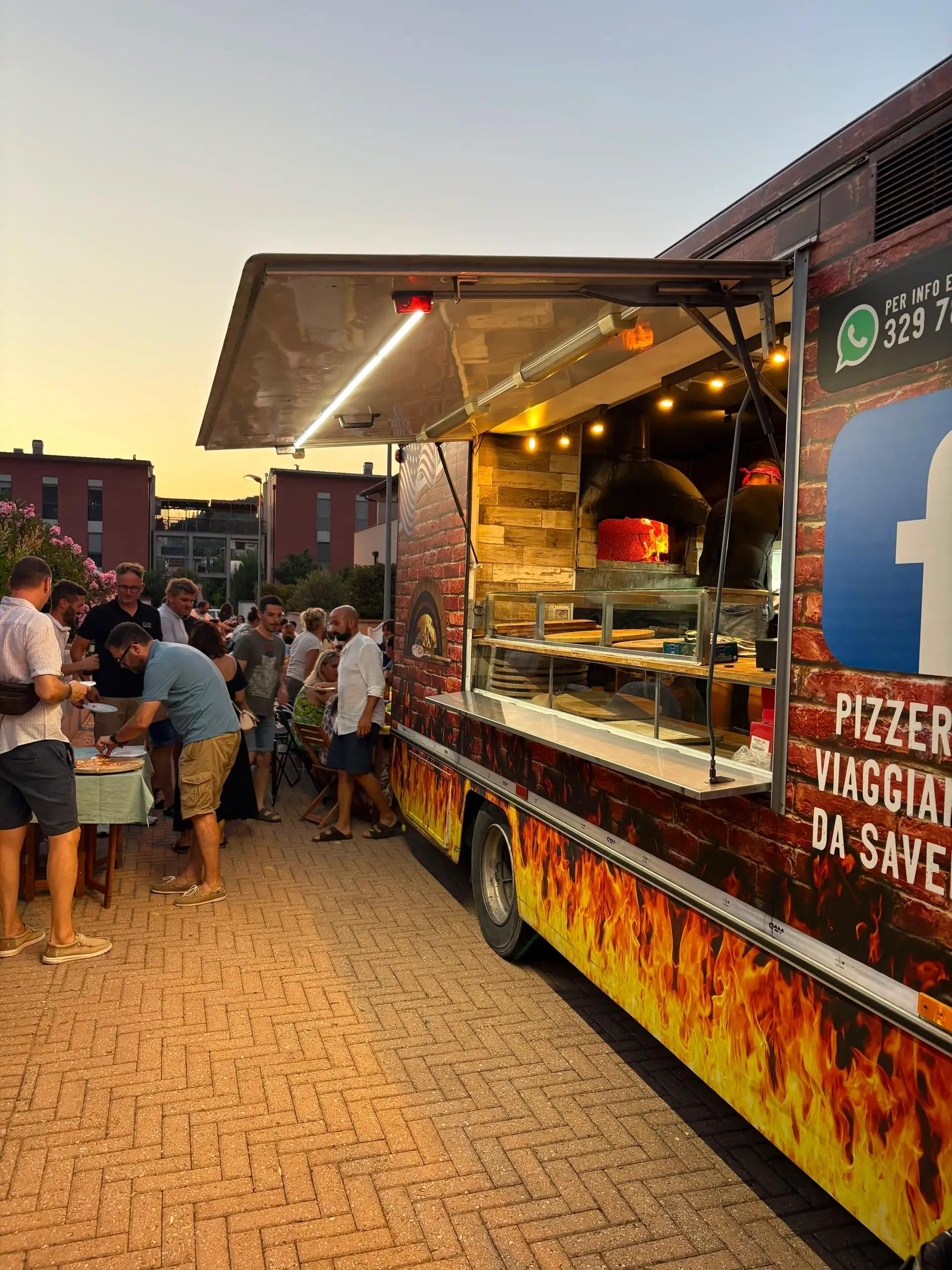 Il camion aperto al tramonto, con il forno acceso e le persone al banco
