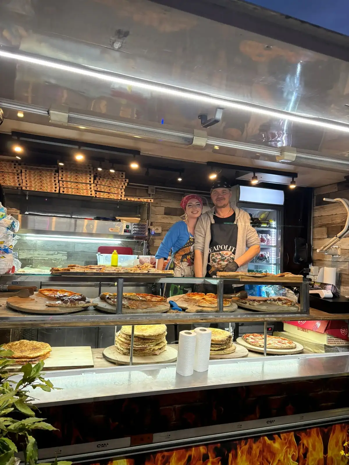 Due pizzaioli dietro al banco carico di pizze e schiacciate