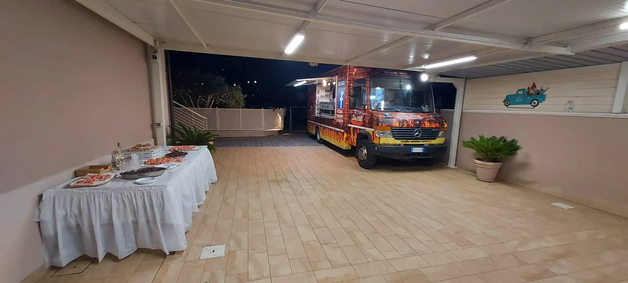 Il camion sotto una tettoia, di sera, con il buffet apparecchiato accanto